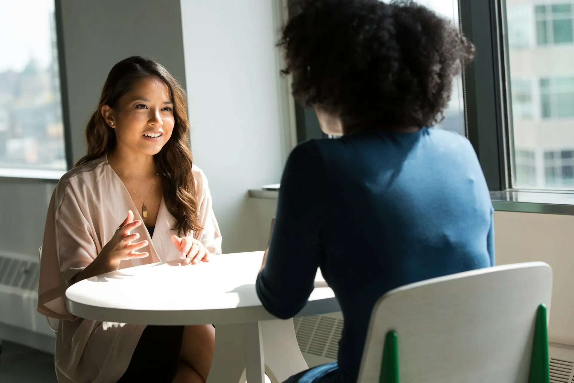 Consultora conversando com uma cliente em uma mesa, perto da janela