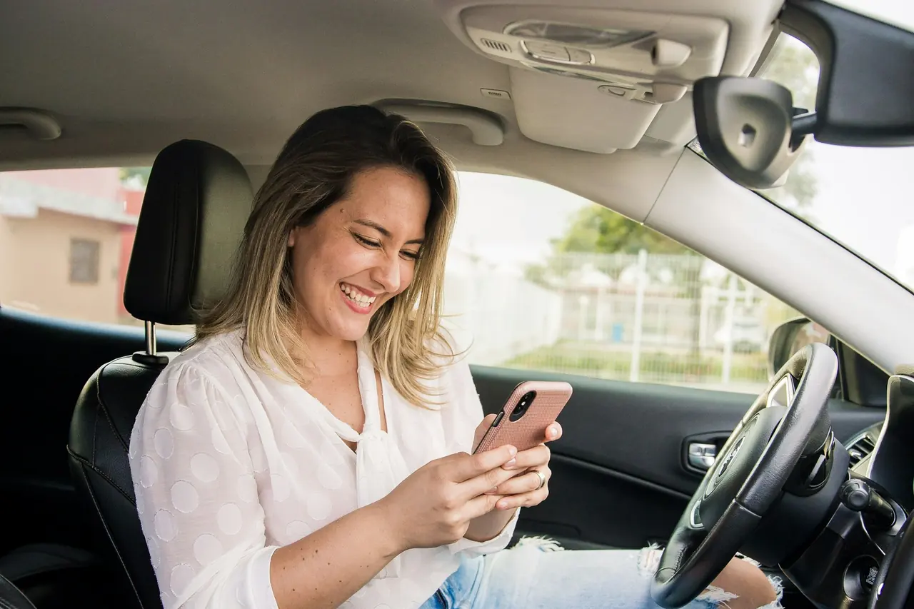 Motorista sorrindo enquanto confere o celular dentro do carro