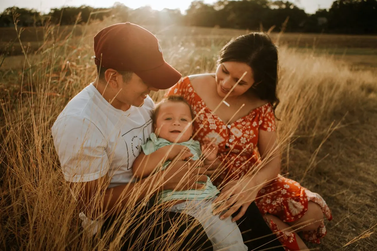 Pai e mãe abraçados ao bebê em um campo ao pôr do sol
