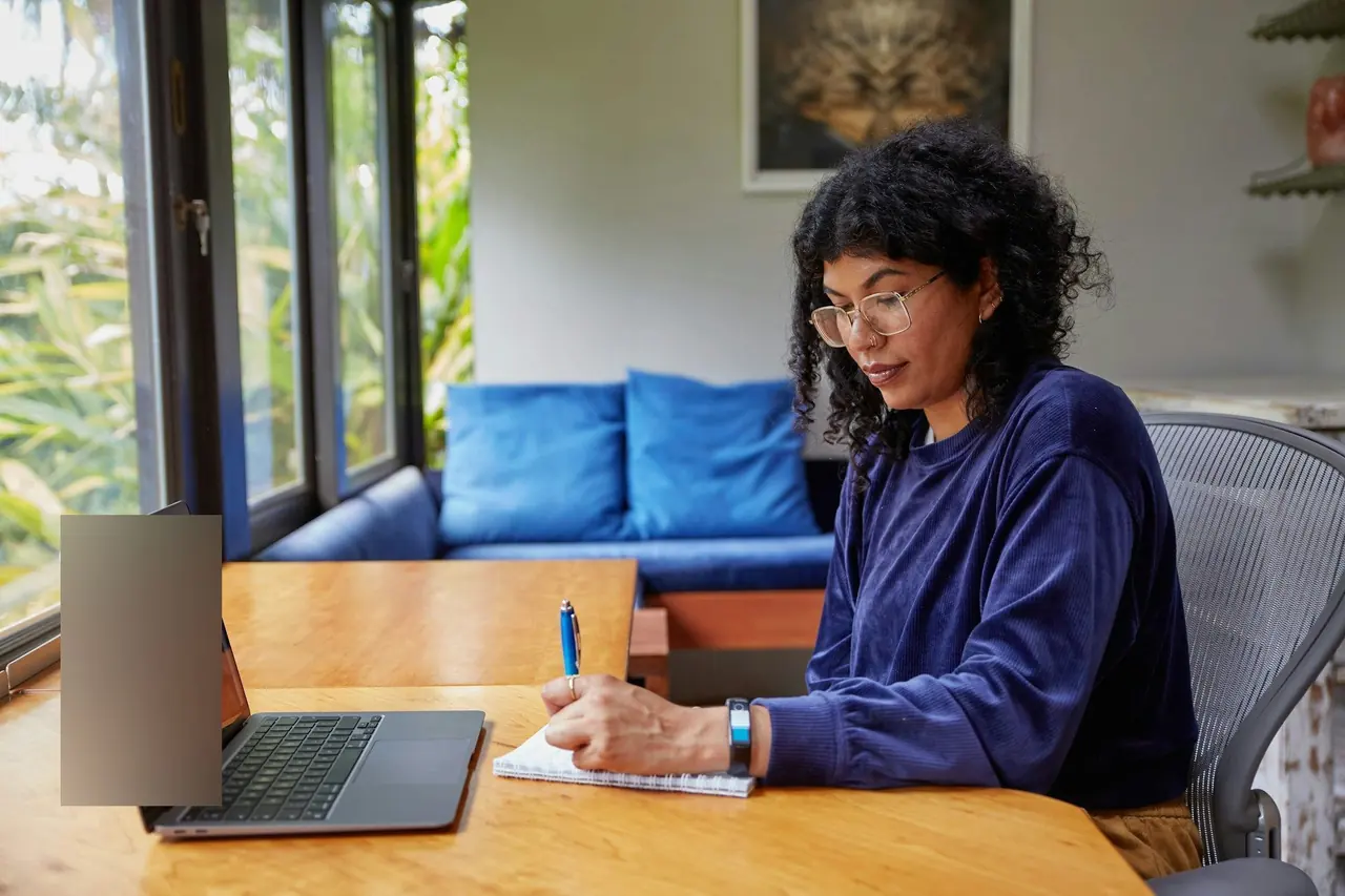 Mulher fazendo anotações ao lado do notebook em casa