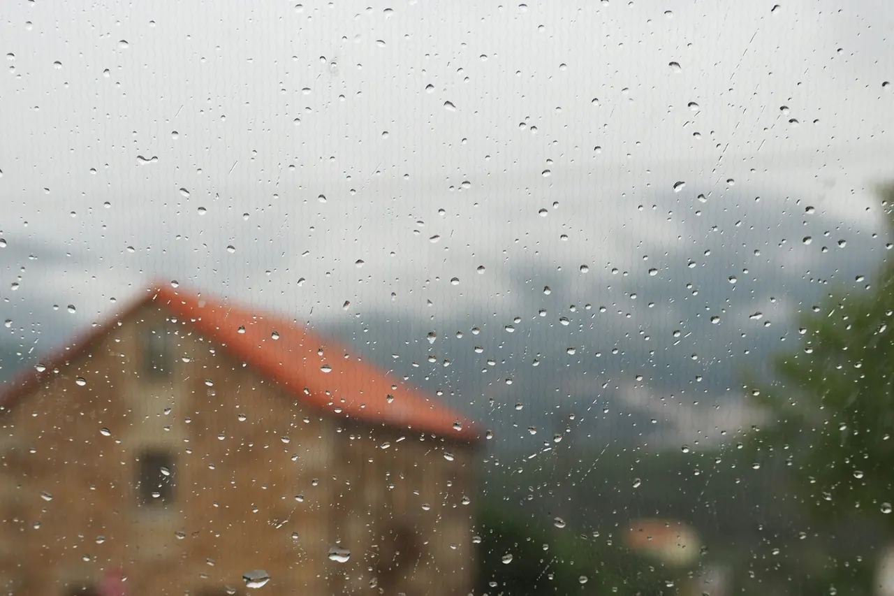 Casa de telhado vermelho vista através de uma janela molhada de chuva