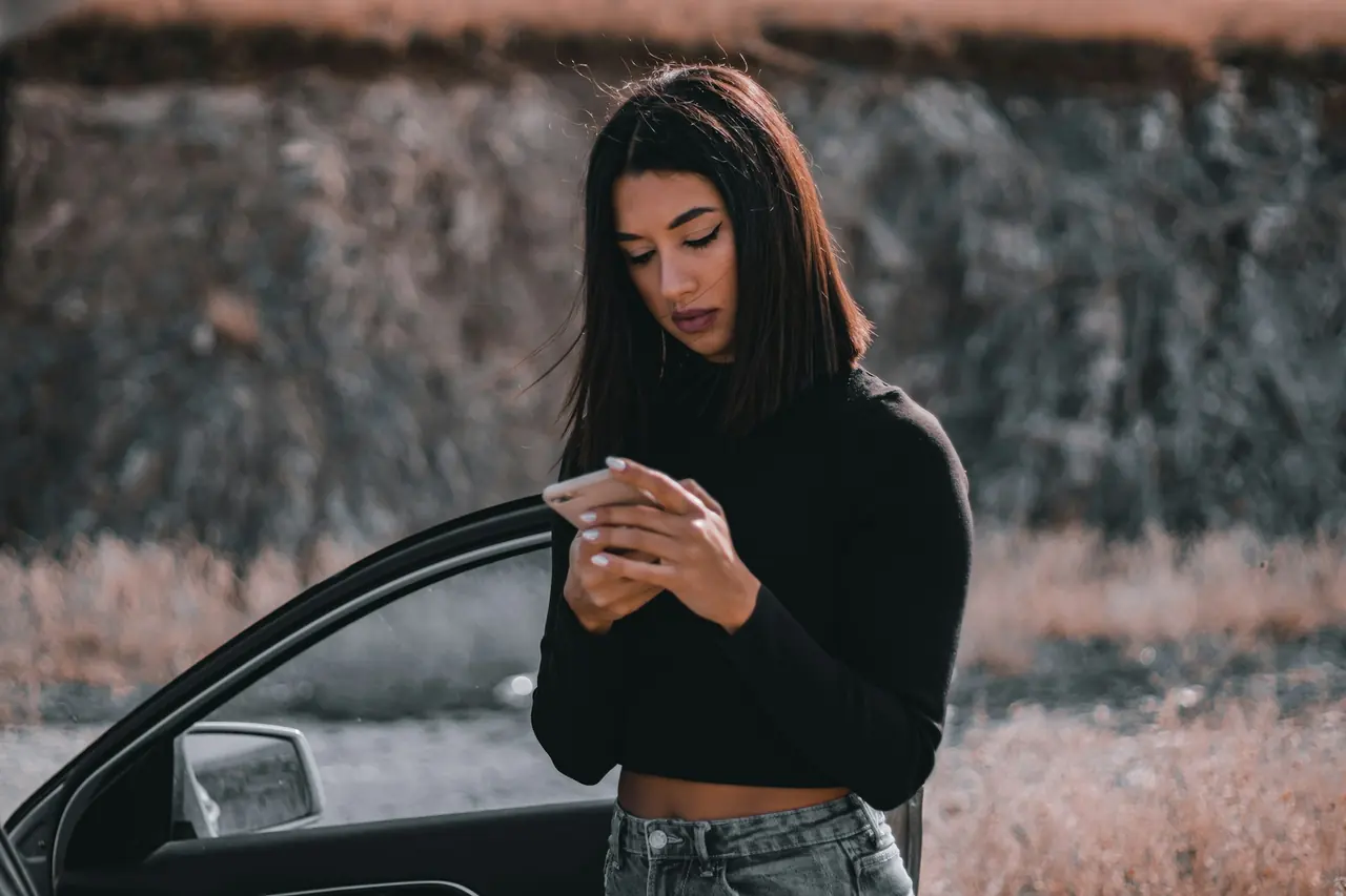 Mulher ao lado do carro pesquisando no celular
