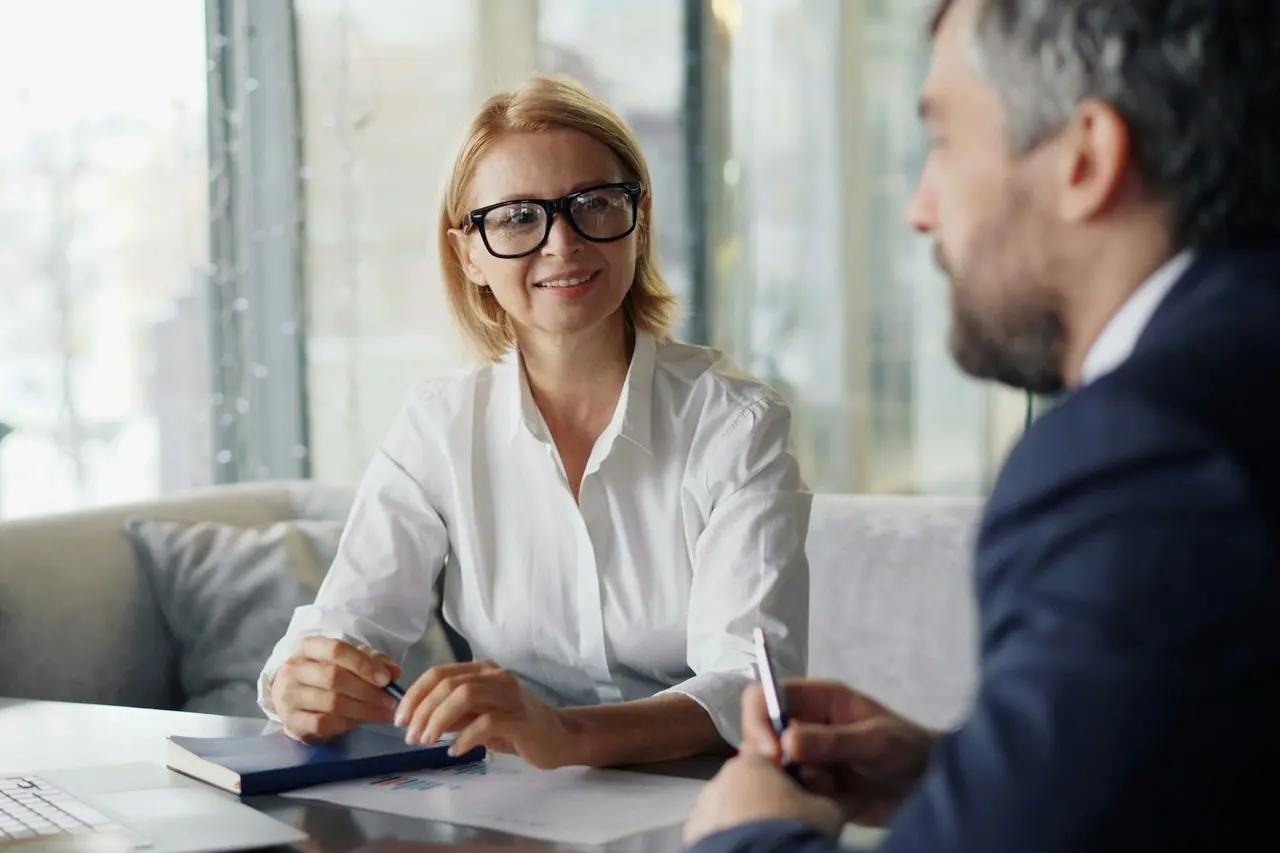 Mulher sorridente conversando com um consultor em uma mesa de reunião