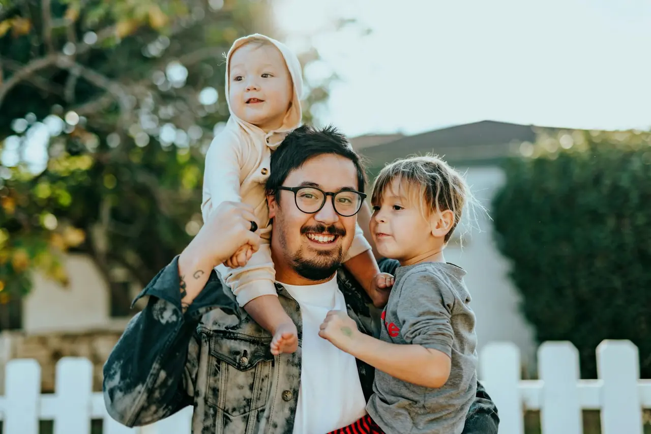 Pai sorridente carregando os dois filhos pequenos