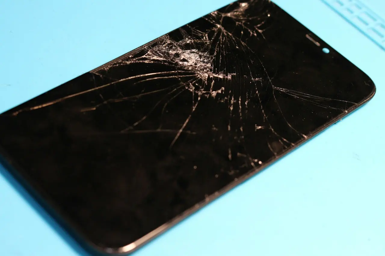 Celular com a tela trincada sobre uma mesa azul