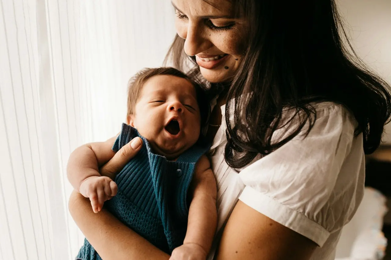 Mãe sorrindo com o bebê no colo em casa