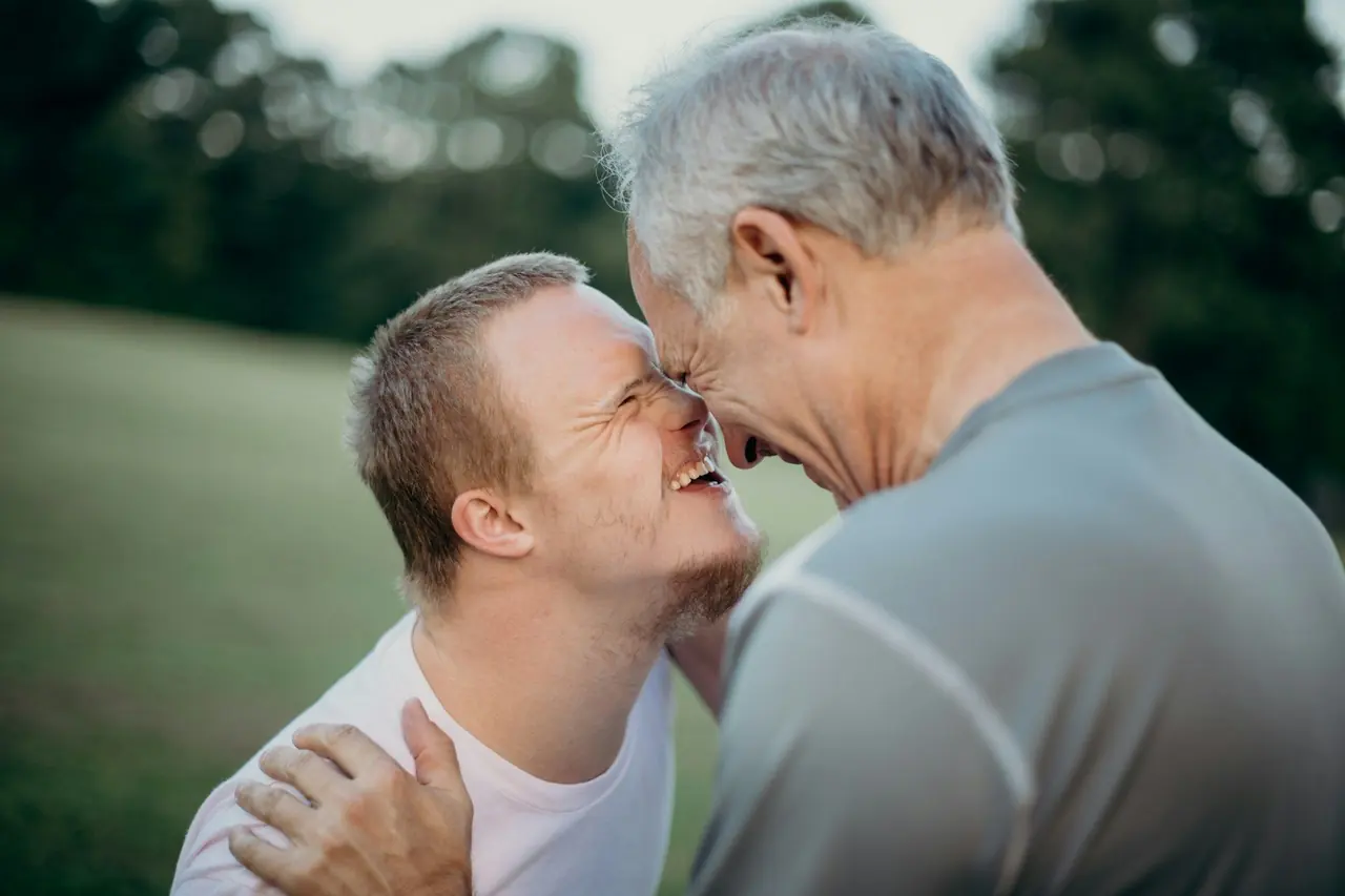 Pai e filho adultos sorrindo testa com testa ao ar livre