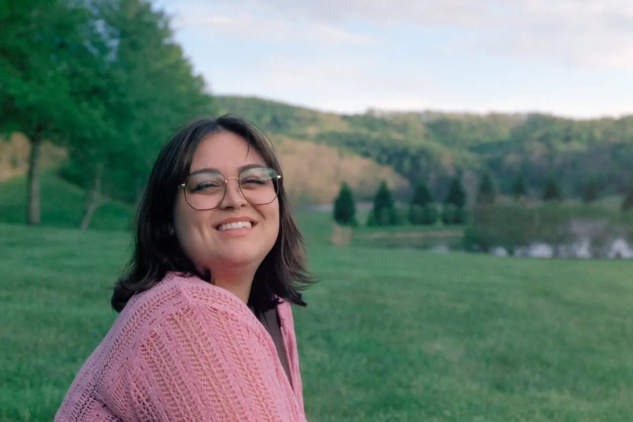 Mulher sorridente de blusa rosa em um campo verde