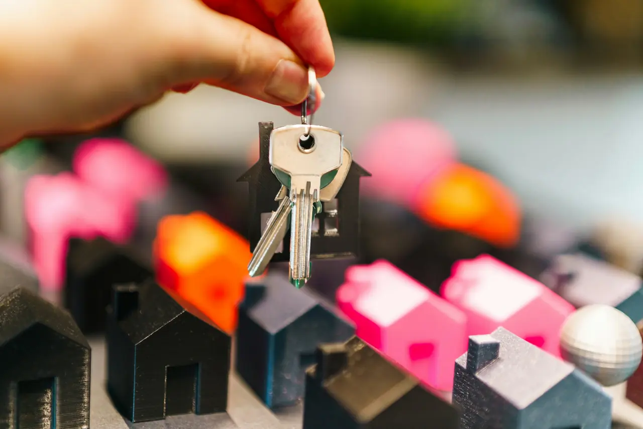 Mão segurando chaves de casa sobre miniaturas de casas coloridas