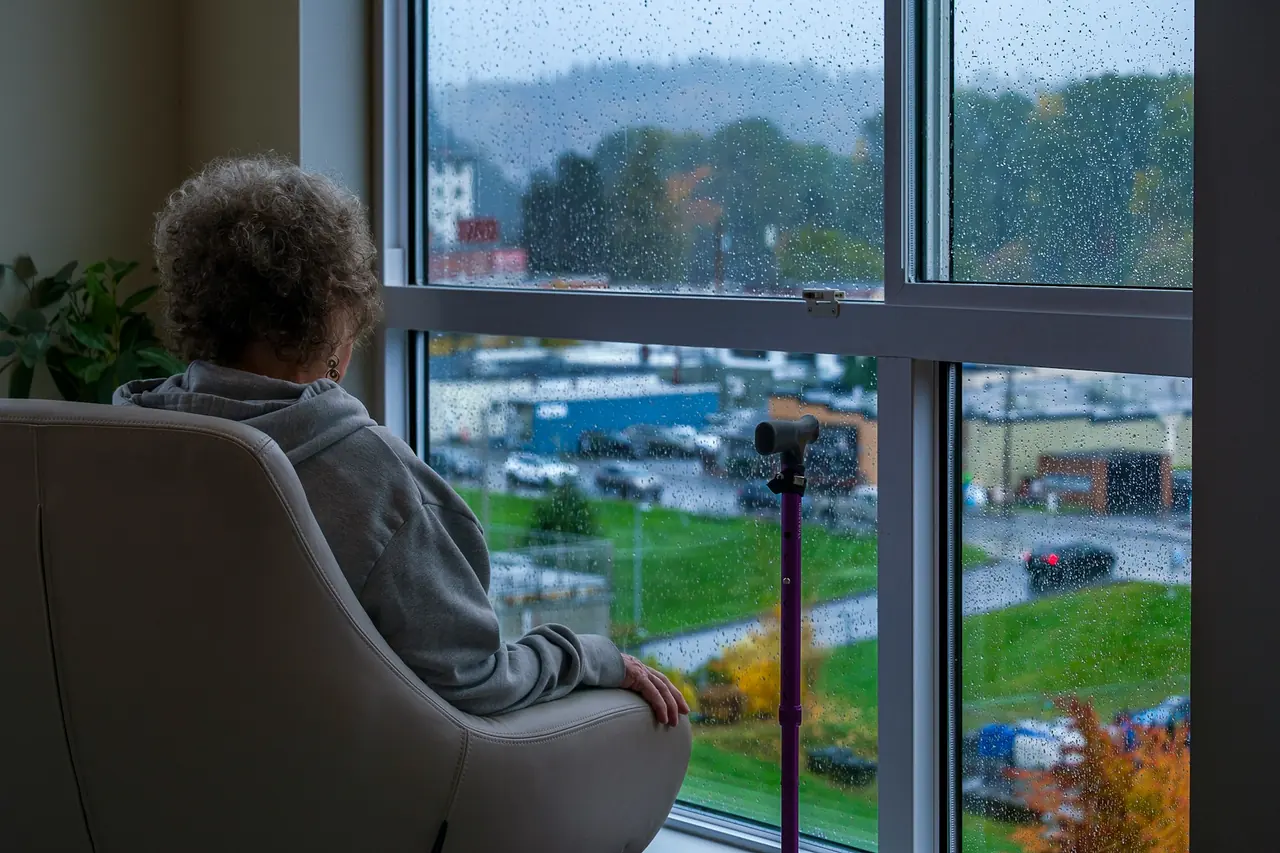 Mulher na poltrona olhando a chuva pela janela de casa