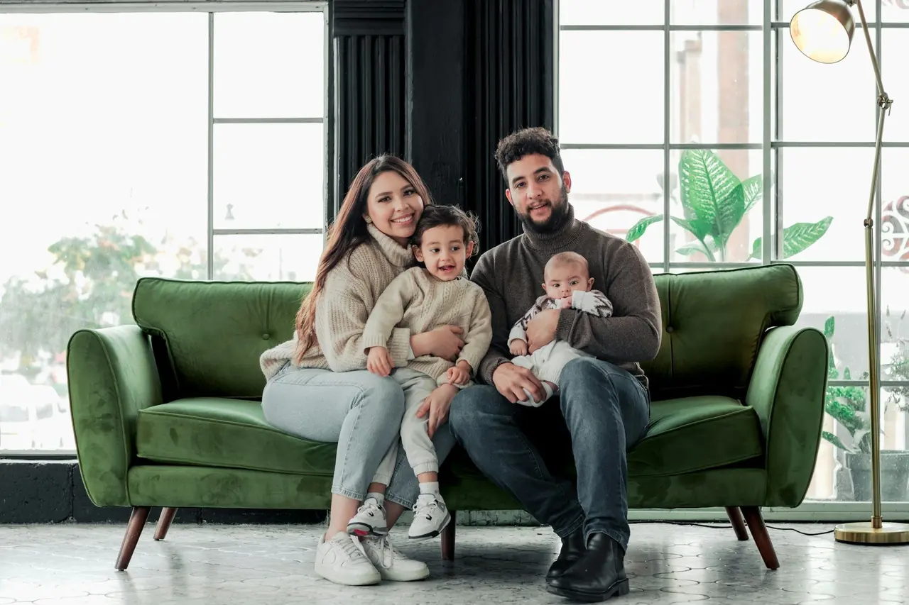 Pai, mãe e dois filhos pequenos sorrindo em um sofá verde