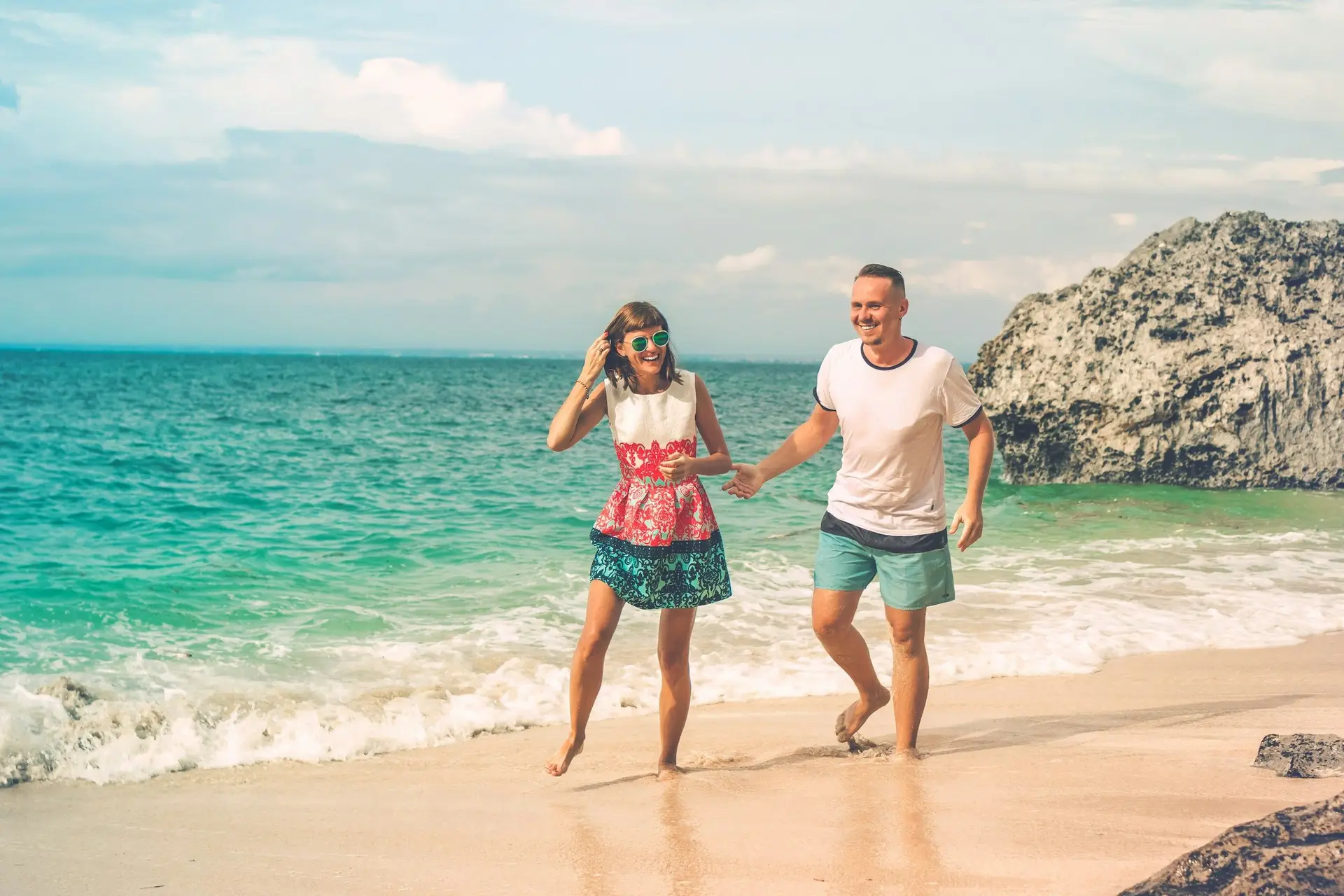 Casal de mãos dadas caminhando na beira do mar em uma praia ensolarada